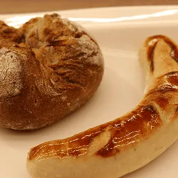 Gebratene Bratwurst neben einem rustikalen Wecken auf einem weißen Teller