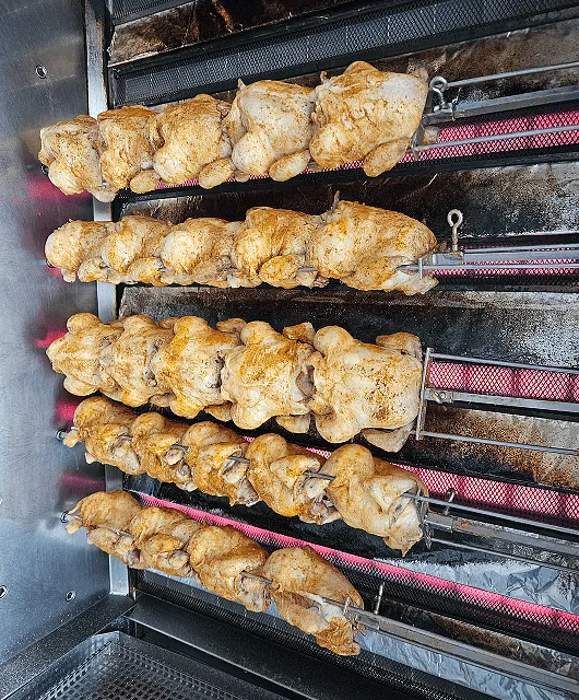 Mehrere Hähnchen am Drehspieß in einem Grill, gleichmäßig gebräunt und rotierend