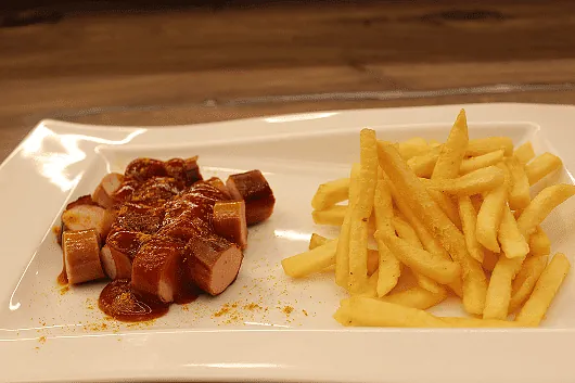 Currywurst in Scheiben mit Currysauce und Pommes Frites auf weißem rechteckigem Teller