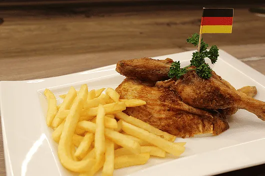 Hähnchenteile mit Pommes Frites auf weißem Teller, garniert mit Petersilie und deutscher Flagge