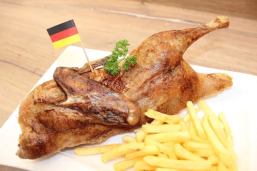 Knusprig gebratenes Hähnchen mit Pommes Frites auf weißem Teller, dekoriert mit kleinem Deutschland-Flaggenstäbchen und Petersilie