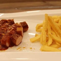 Currywurst in Scheiben mit Currysoße und einer Portion Pommes Frites auf weißem Teller